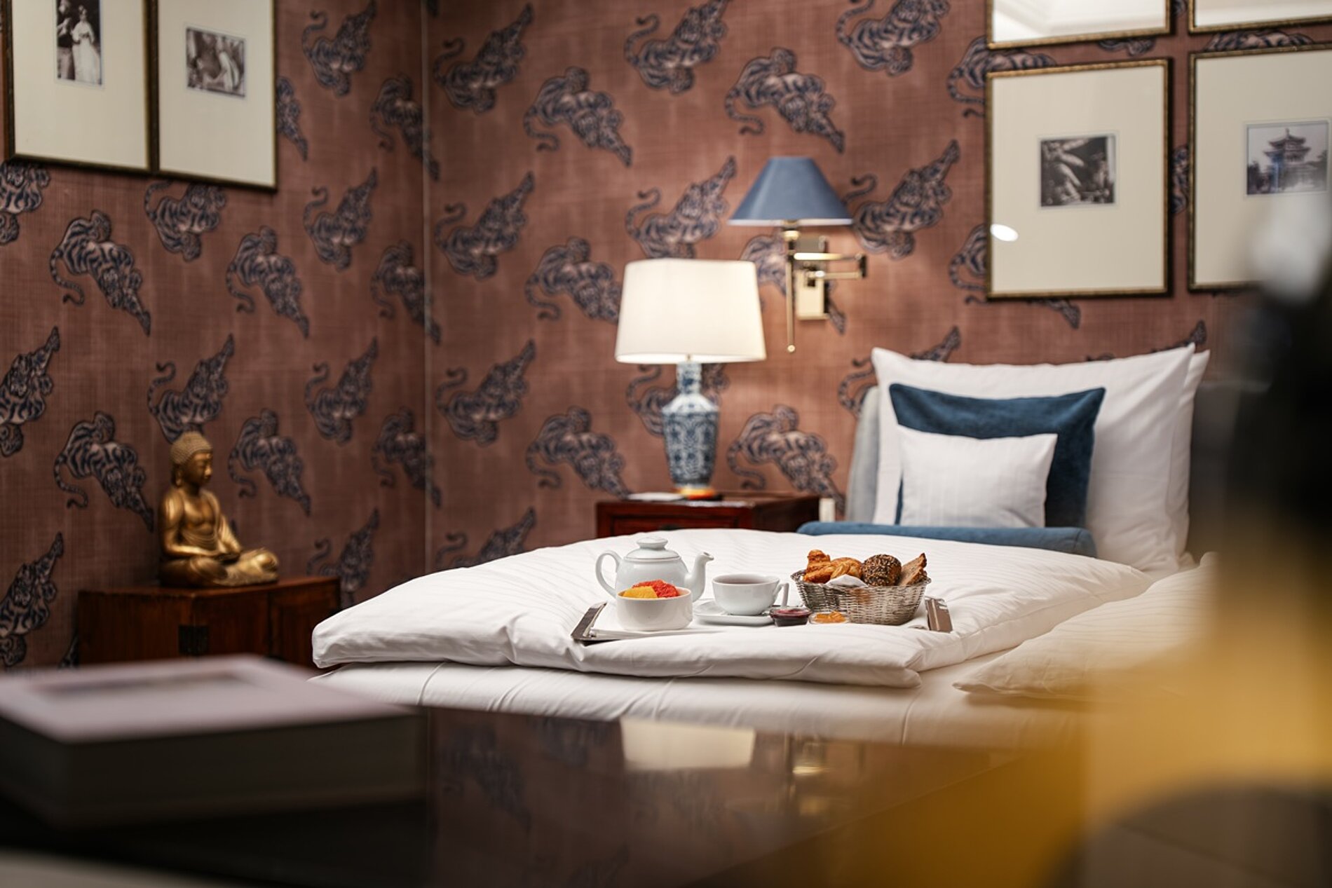 Stilvolles Hotelzimmer_Frühstück auf dem Bett_braune Tapete mit Tigermuster und helle Bettwäsche